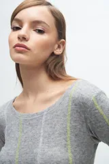 Remera gris de corte ajustado, con cuello redondo y mangas largas. Presenta líneas verticales bordadas en color verde claro y blanco.