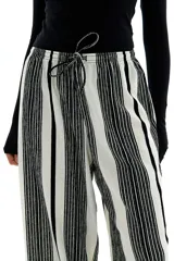 Pantalón palazzo de punto con textura a rayas verticales en blanco y negro. Tiene tiro alto, piernas rectas, elástico en la cintura y cordón para ajustar.