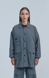 Campera gris con broches en el delantero, forrada con red, múltiples bolsillos con detalles en réflex y puños elásticos en las mangas. Confeccionada en textil liviano 100% poliéster y calce oversize.