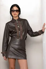 Camisa de cuero marrón con cuello clásico, botones metálicos al frente y volados de gamuza al tono en el pecho y puños.