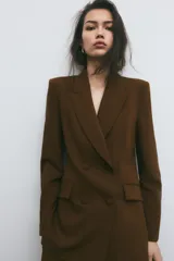 Blazer marrón de cuello solapa y manga larga. Bolsillos con solapa en delantero y cierre frontal cruzado con botones forrados.