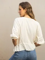 Blusa color crema de viscosa con cuello redondo y abertura central con botones. Tiene mangas 3/4 con puños fruncidos, detalles calados y bordados en mangas, delantera y espalda. La cintura tiene un lazo de ajuste.