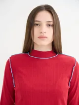 Polera negra de tela rib con cuello alto y mangas largas. Presenta pespuntes rojos en cuello, hombros y puños.