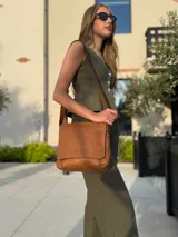 Bandolera de hombro color gris claro, con solapa frontal y correa ajustable. Presenta un diseño simple y práctico, ideal para uso diario.