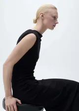 Vestido midi negro sin mangas, con cuello asimétrico, diseño entallado y cintura drapeada.