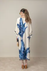 Vestido largo color natural con estampado de hojas de palmera en tonos verdes. Tiene corte amplio tipo túnica, cuello redondo, mangas tres cuartos, bolsillos laterales y ruedo con ribete.