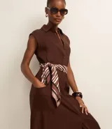 Vestido chemise de lino color negro, con cuello camisero, sin mangas y cierre frontal con botones. Incluye cinturón de tela estampado.