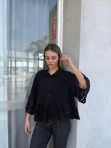 Camisa negra con cuello clásico, cierre frontal con botones, mangas 3/4 con detalle de calado y ruedo con volados y calado.