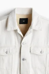 Campera de denim color crudo, de corte recto, con cuello clásico, cierre frontal con botones metálicos, bolsillos con solapa en el pecho y bolsillos laterales.