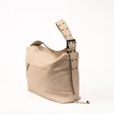 Bolso tipo hobo color beige con textura granulada y correa de hombro ajustable. Cierre superior con cremallera y tiras decorativas laterales con detalle de nudo.