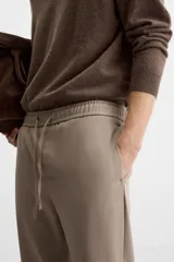 Pantalón color arena de corte recto, confeccionado en tejido elástico. Cuenta con cintura elástica ajustable con cordón, bolsillos laterales y bolsillos de vivo en la parte trasera.