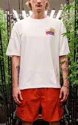 Remera blanca de corte extra oversize con hombros caídos, cuello redondo de rib al tono y estampado con dibujos de plantas de marihuana en estilo cómic.