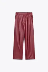 Pantalón de cuero sintético color bordó, de tiro medio, corte recto y cintura cruzada con trabillas. Cuenta con bolsillos laterales, pinzas delanteras y cierre frontal con cremallera, botón y gancho metálico.