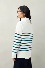 Polera blanca de punto con cuello alto y cierre metálico, de calce relajado y diseño a rayas horizontales azules.