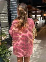 Camisa oversize de manga corta con cuello camisero, confeccionada en tejido de viscosa y lino. Presenta un diseño estampado de estilo patchwork, dividido verticalmente en dos mitades: una en tonos amarillos y marrones, y la otra en tonos rosados y morados.