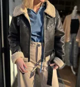 Campera de cuero sintético color marrón oscuro con interior de piel sintética color beige. Tiene cuello con solapas, cierre frontal con cremallera, bolsillos laterales con cremallera y cinturón ajustable en la cintura.
