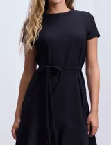 Vestido corto negro texturado con escote redondo, manga corta, lazo de ajuste en la cintura y ruedo con volados.