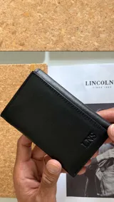 Billetera de cuero negra con diseño vertical de tres cuerpos, dos divisiones para billetes, ocho espacios para tarjetas y un visor.