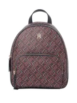 Mochila de silueta clásica con estampado integral de monograma en tonos marrón oscuro y blanco. Presenta un compartimento principal con cierre, un bolsillo exterior con cremallera y un asa superior negra. El logo TH metálico se encuentra centrado en el frente.