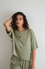 Remera de manga corta color crema, con textura acanalada y cuello redondo. Presenta un pequeño parche bordado con un diseño floral o geométrico en el pecho.