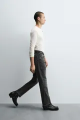 Pantalón de jean celeste de corte flare, con tiro medio, cinco bolsillos, cierre frontal con cremallera y botón, y bajo con acabado irregular.