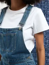 Jumper largo de denim azul con breteles regulables, bolsillos frontales y corte recto.
