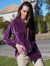 Camisa roja de terciopelo con cuello clásico, botones frontales y mangas largas con puños abotonados. Tiene dos bolsillos de parche en el pecho.