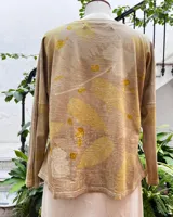 Remera de manga larga color beige con estampado botánico verde y amarillo, escote en V, corte ajustado y tajos laterales.