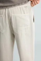 Pantalón color arena de corte recto, confeccionado en tejido de algodón y lino. Cuenta con cintura elástica ajustable con cordón, bolsillos delanteros y traseros de parche.