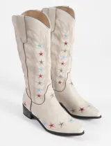 Botas tejanas de cuero vegano color crema con bordados de estrellas rojas y azules.