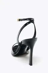 Sandalias negras de charol con efecto craquelado, de tacón fino y punta cuadrada. Cierre con hebilla metálica en la pulsera del tobillo.