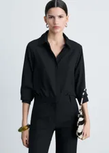Camisa negra de tejido fluido con cuello camisero, cierre frontal con botones y mangas largas con puños abotonados.