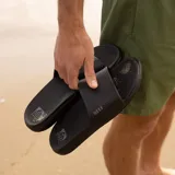 Sandalias Reef tipo ojotas, color negro, con tira ancha sobre el empeine y logo de la marca.