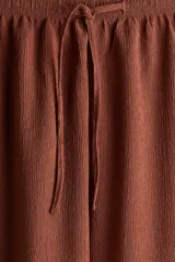 Pantalón marrón de punto texturado, corte holgado, tiro alto, piernas rectas, elástico en la cintura y cordón para ajustar.