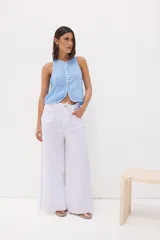 Top sin mangas color beige, con escote en V y cierre frontal de botones de nácar. Presenta costuras decorativas en el borde del escote y sisas.