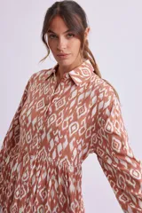 Vestido camisero midi color marrón con estampado geométrico en blanco, de corte recto, con cuello camisero, abotonadura frontal y mangas largas con puños abotonados.