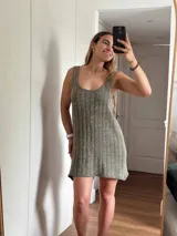 Vestido corto de tejido de punto color beige/dorado, con escote redondo y tirantes anchos. Presenta un tejido acanalado verticalmente con hilos de lurex que le dan brillo.