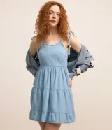 Vestido corto de jeans celeste, con breteles finos con lazos, escote en U, espalda descubierta y falda de tres niveles con volados.