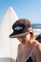 Gorra de cinco paneles color marrón de pana, con visera plana y parche bordado con el logo de la marca "Glassy" en el panel frontal.