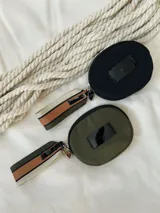 Monedero negro circular con cierre de cremallera y llavero de cinta estampada a rayas.