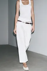 Pantalón cropped color beige de tiro alto y corte recto, confeccionado en algodón. Cuenta con bolsillos delanteros y traseros, trabillas en la cintura y cierre frontal con cremallera y botón.