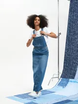 Jumper largo de denim azul con breteles regulables, bolsillos frontales y corte recto.