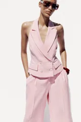 Chaleco rosa con cuello halter y escote pico con solapa. Espalda descubierta. Bolsillos delanteros con solapa. Cierre frontal cruzado con botones.