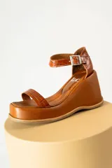 Sandalias de cuero color marrón con plataforma y taco de cuña. Tiras anchas con textura tipo cocodrilo y hebilla metálica plateada.