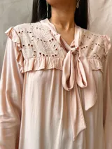 Camisa color rosa pálido con cuello babero bordado con calados y volados, mangas largas y lazo en el escote.