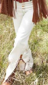 Pantalón de jean blanco con corte acampanado, cintura alta, detalles trenzados y aplicaciones de cuero en la parte inferior.