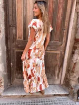 Vestido largo con estampado abstracto en tonos camel, naranja y blanco, con escote en V, mangas cortas con volados y falda con volados en el ruedo.