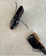 Zapato acordonado de cuero vacuno color marrón con aberturas laterales y cordones negros.
