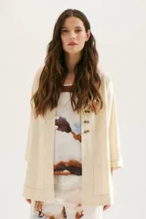 Sobrecamisa beige de corte recto, cuello mao y mangas 3/4. Presenta cierre frontal con botones de madera y bolsillos laterales.