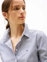 Camisa de popelina a rayas verticales azules y blancas, de corte regular, con cuello inglés y puños con botón. Logo de Tommy Hilfiger bordado en el pecho.